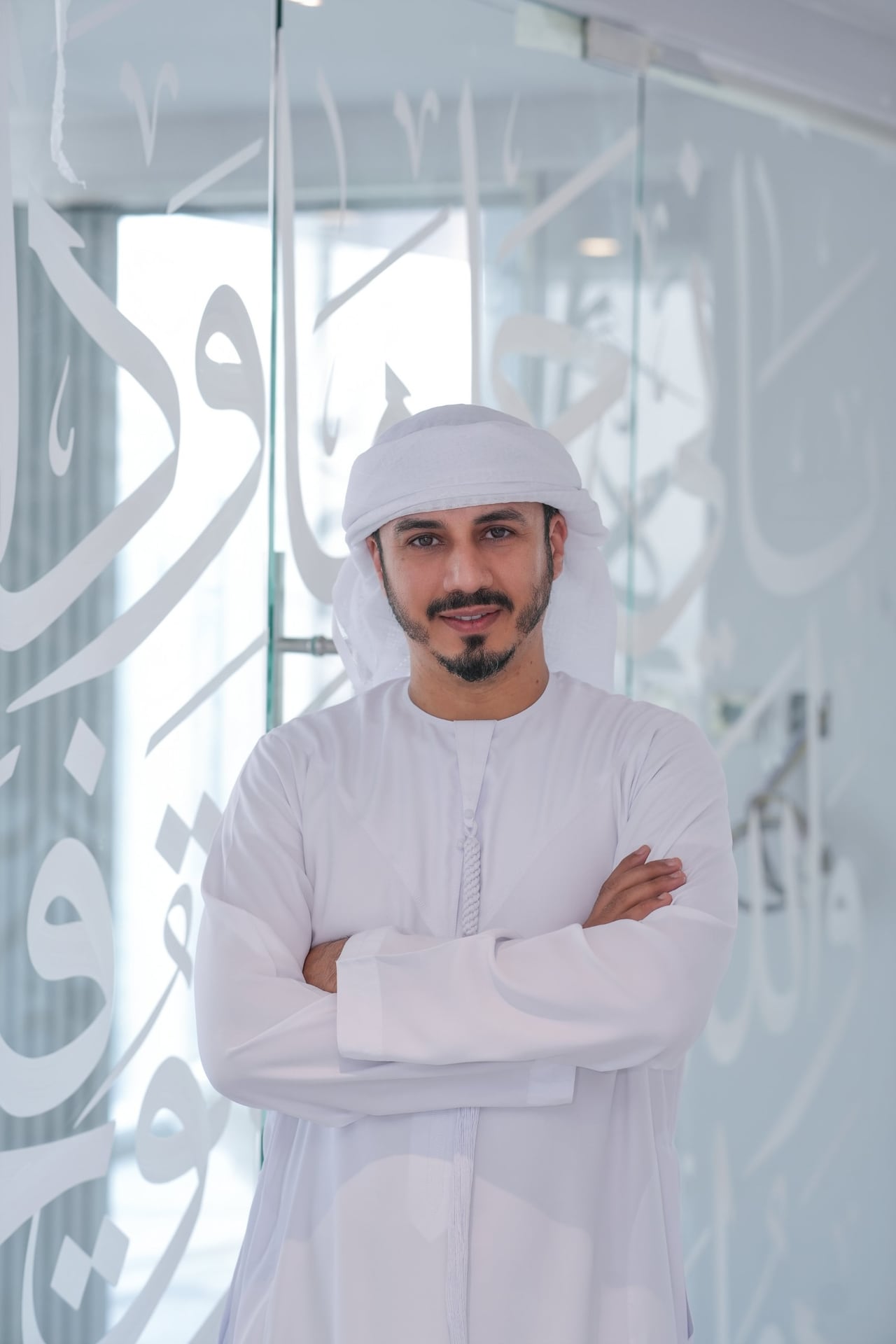 محمود العبادي بالزي الإماراتي، مكتوف اليدين، أمام زجاج تتخلله حروف عربية بيضاء