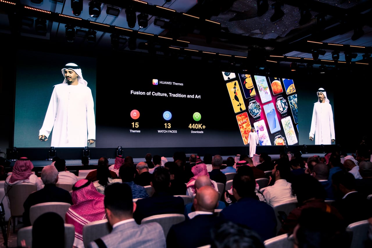 قاعة مؤتمرات مزدحمة، وعلى الشاشة مجموعة من الثيمات وواجهات الساعات وصورة المتحدث